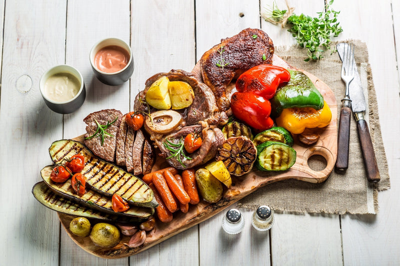 Keto party platter with grilled meats, bell peppers, zucchini, and sugar-free dipping sauces on a wooden board.