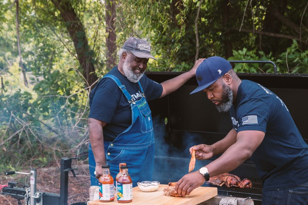 Pitmasters grilling meat on a smoker with True Made Foods BBQ sauce bottles.