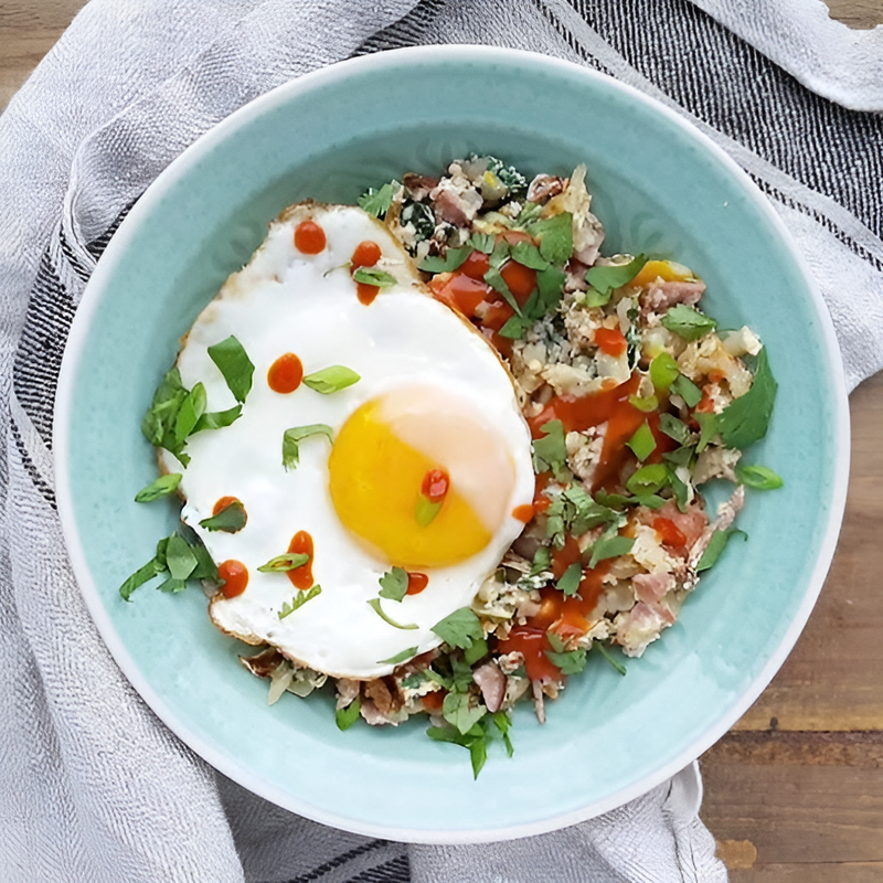  Savory holiday breakfast BBQ hash with potatoes, ham,  and greens topped with a fried egg and True Made Foods BBQ sauce.